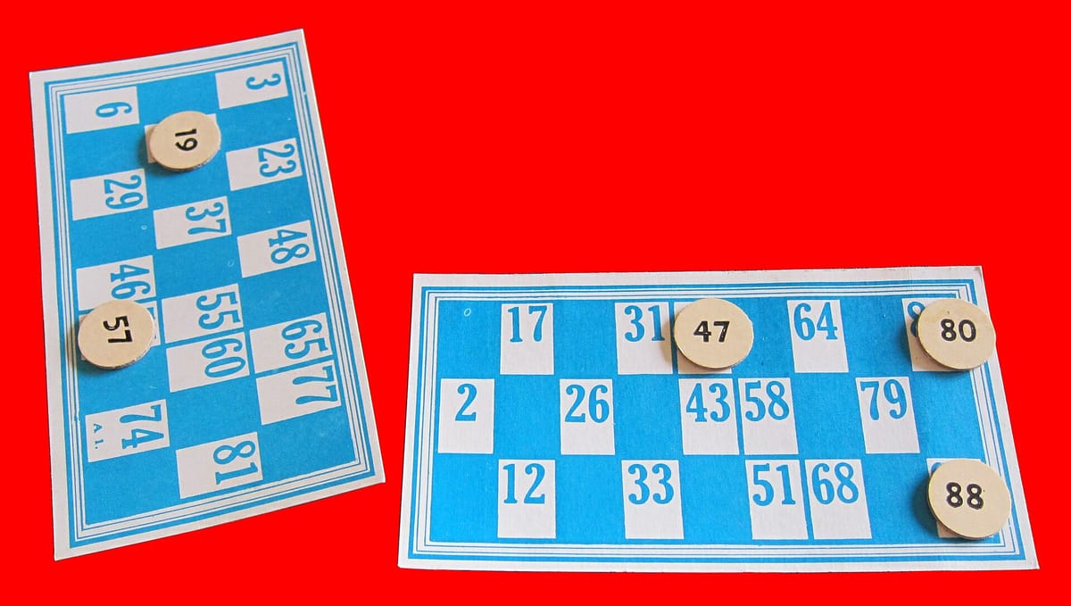 Two blue and white bingo tickets with three rows and nine columns, with wooden counters on some of the numbers, on a red background