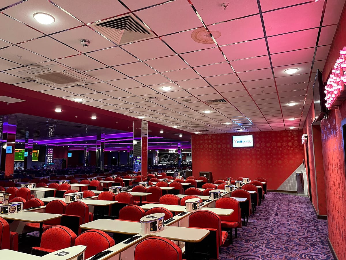 Rows of red chairs and white tables under bright ceiling lights in a large, empty modern bingo hall