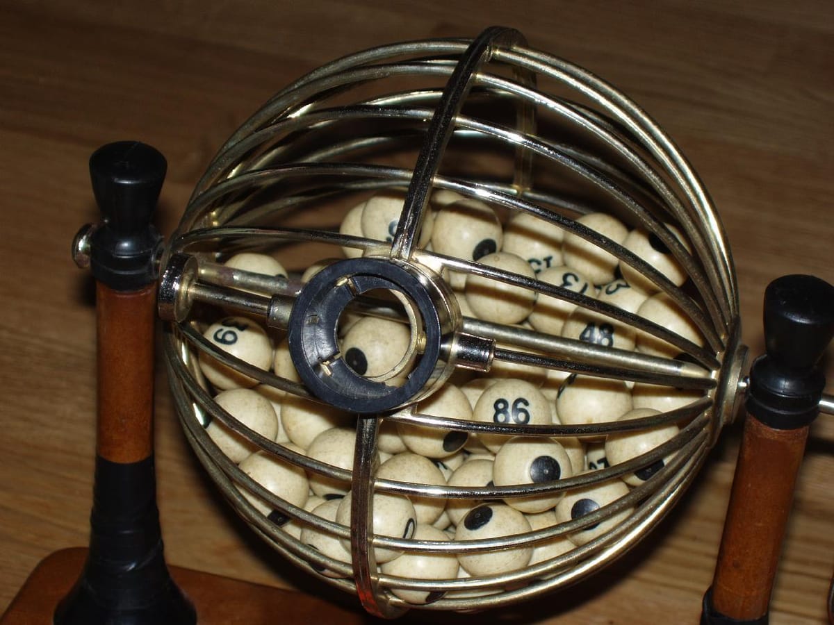 A round wire cage on a wooden stand, full of cream balls printed with black numbers